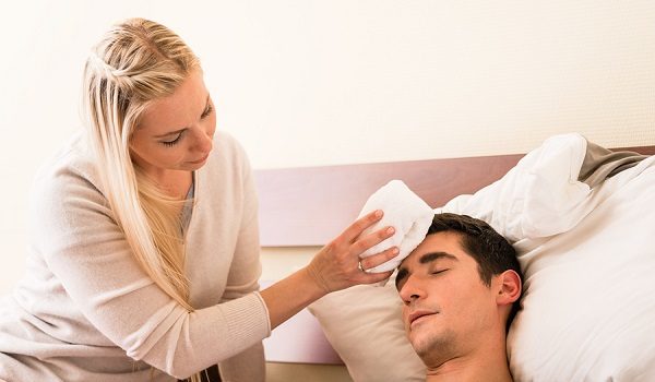Young caring woman holding a cold compress on the forehead of he